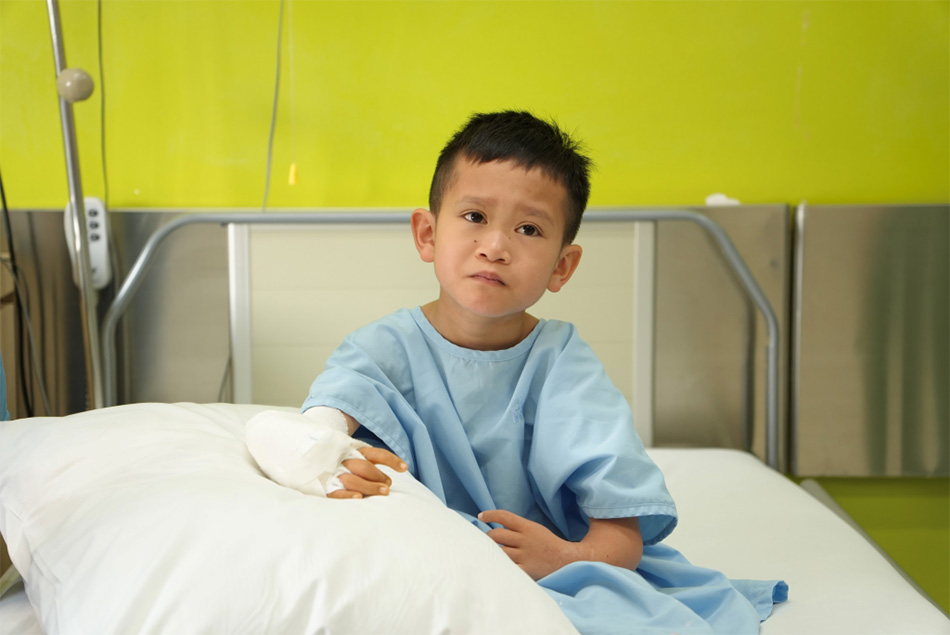 Bé Duy Quang sau khi được phẫu thuật tay phải, đặt bộ khung để kéo xương